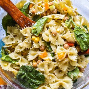 Vibrant and colorful pesto pasta salad with spinach in a clear bowl with wooden serving spoons