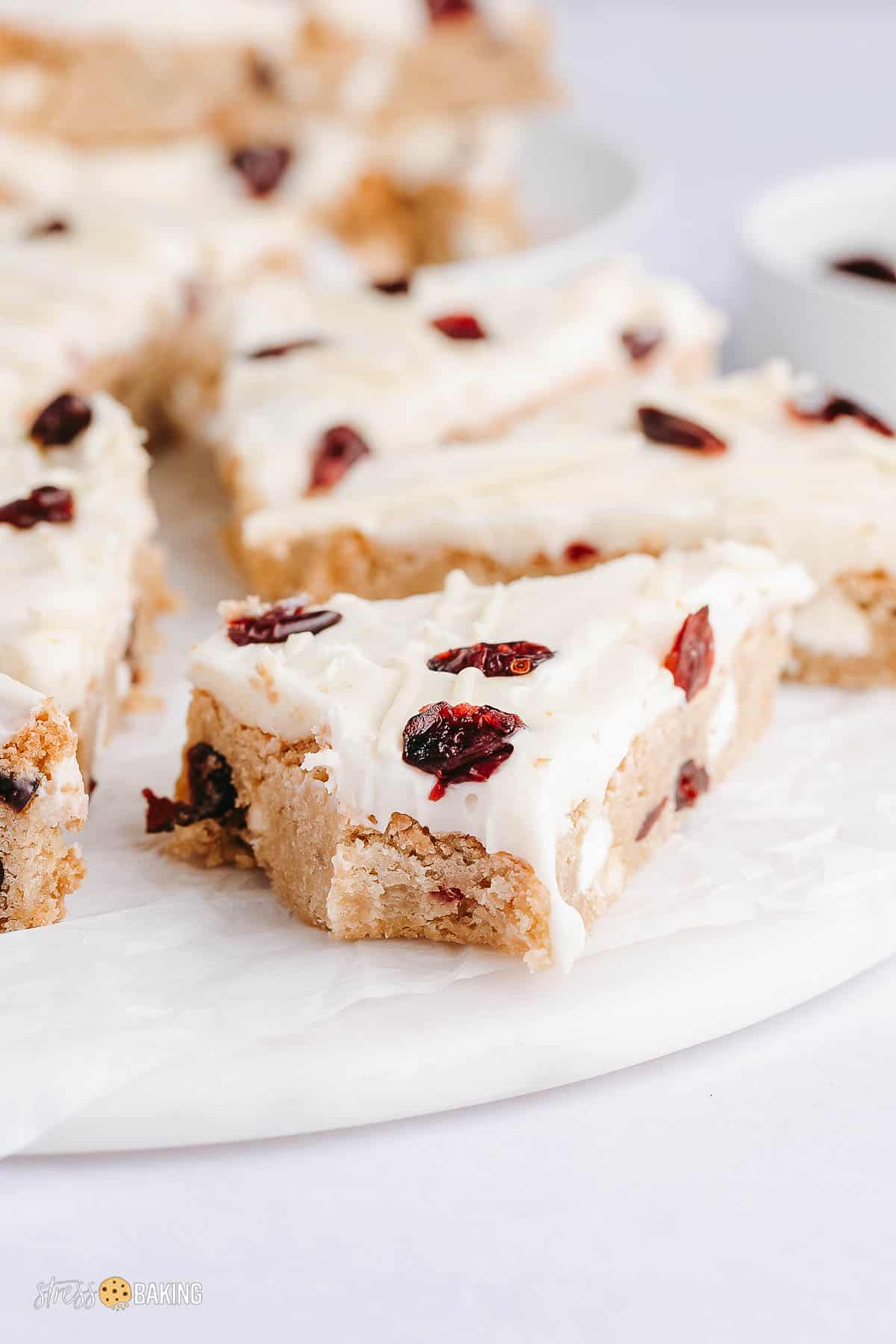 A cranberry bliss bar with a bite taken out of a corner on a white platter