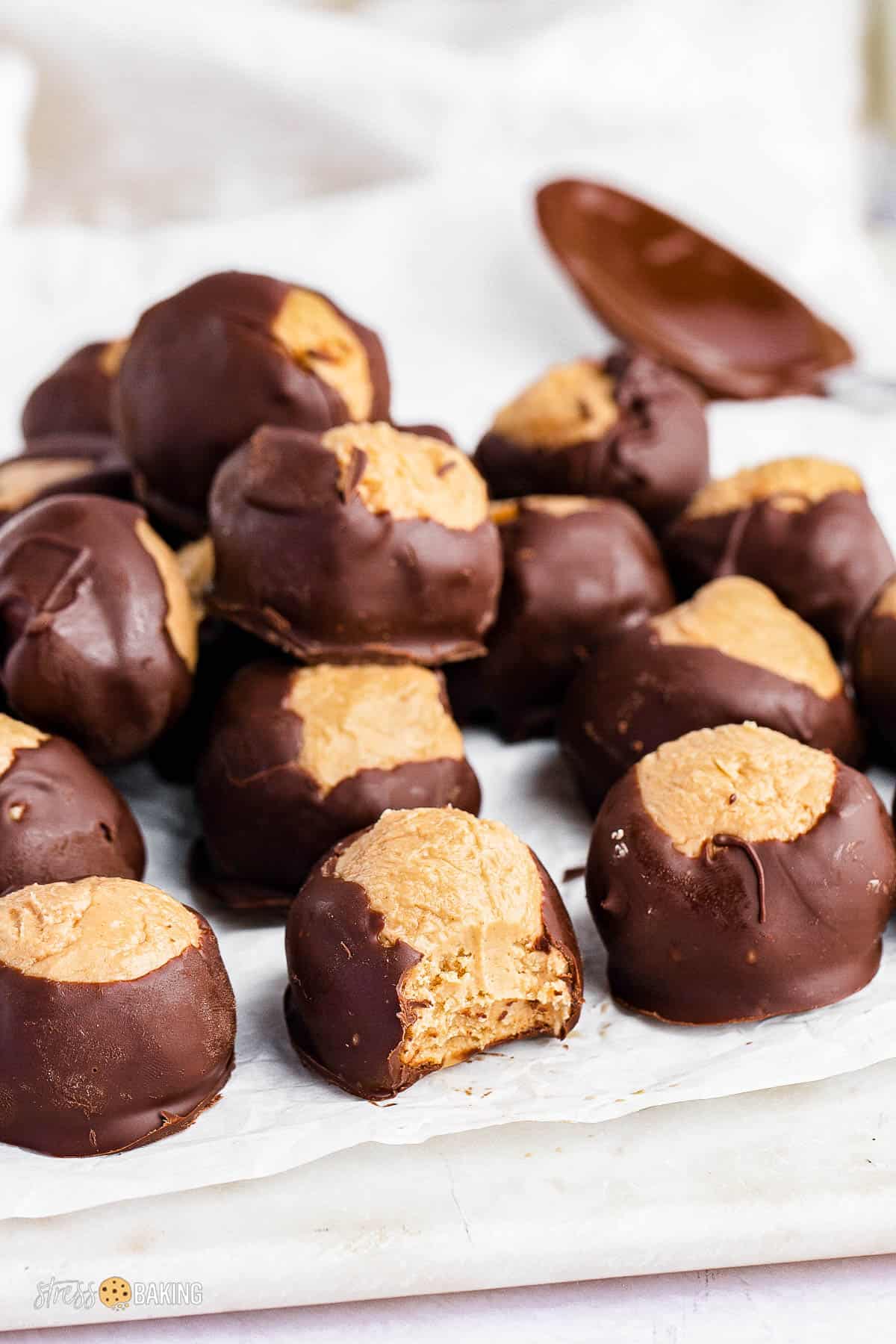 A pile of buckeye balls on parchment paper with a bite taken out of one