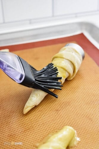 Metal pastry cones wrapped with puff pastry and being brushed with an egg wash