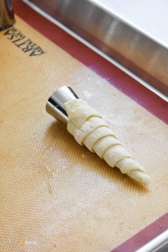 Metal pastry cones wrapped with puff pastry strips on a baking sheet