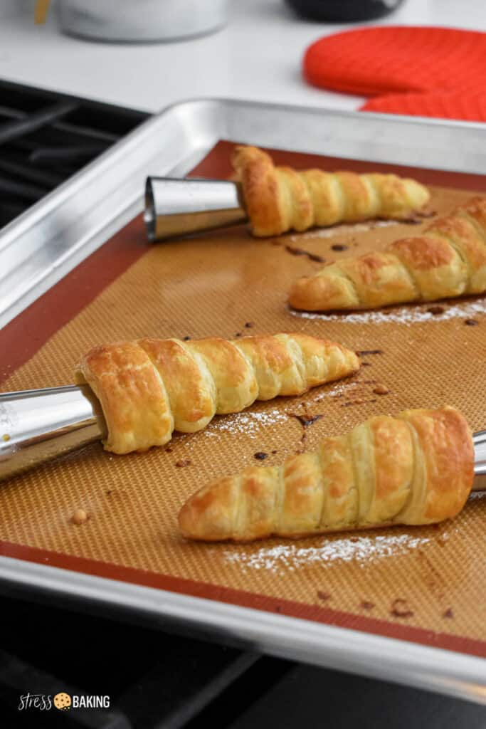 Metal pastry cones with freshly baked pastry on a baking sheet