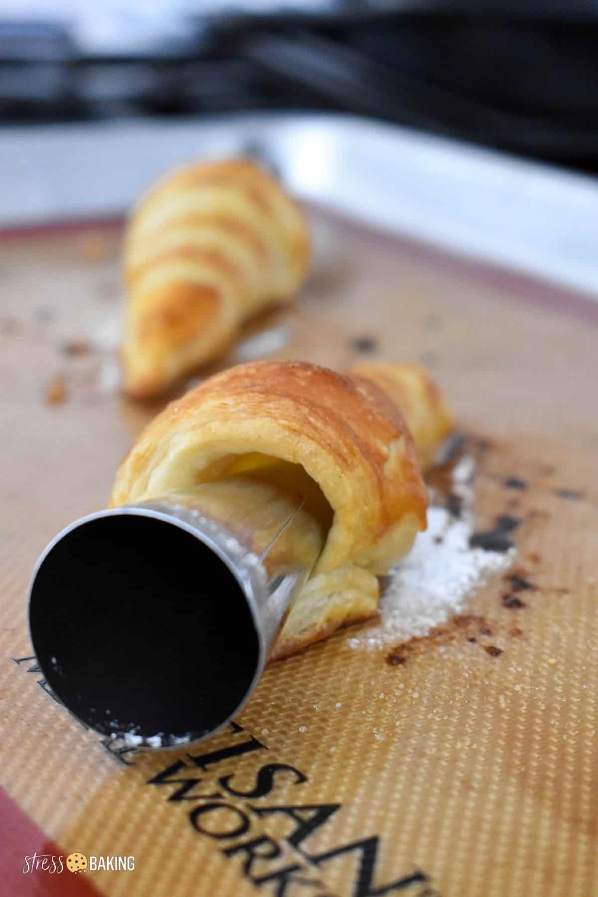 A metal pastry cone sticking out of a tube of golden pastry