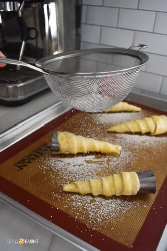 Powdered sugar being dusted on top of pastry cones with a mesh sieve