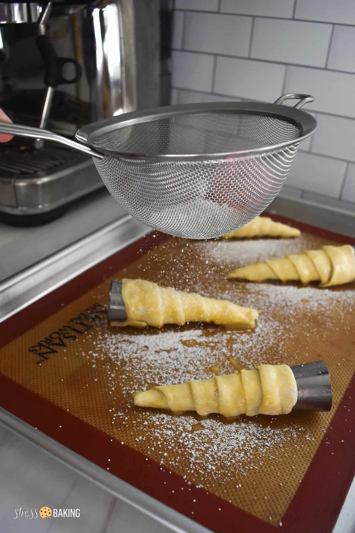 Powdered sugar being dusted on top of pastry cones with a mesh sieve