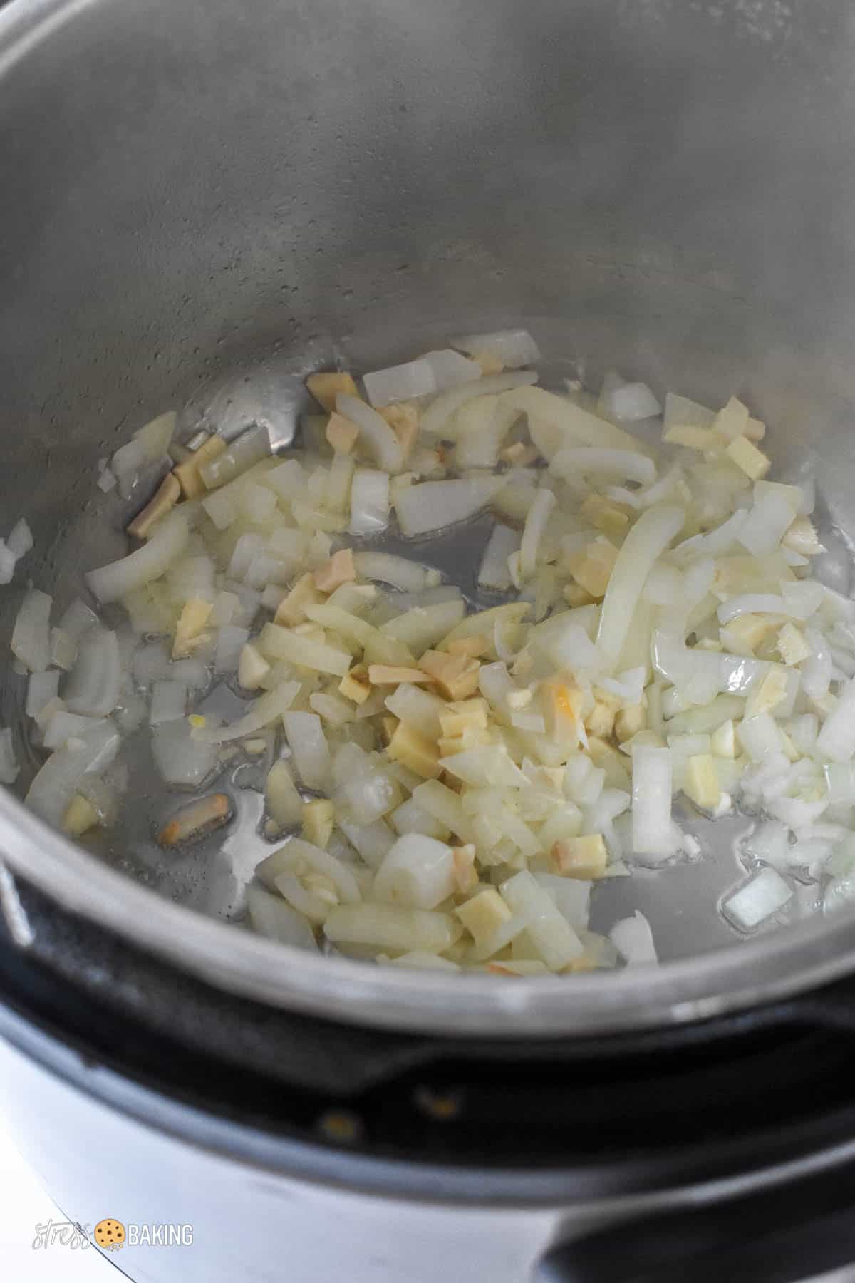 Chopped white onion and ginger cooking in an Instant Pot