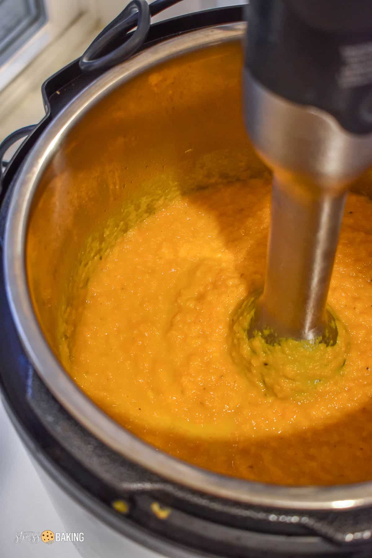 Orange carrot ginger soup being blended with an immersion blender in an Instant Pot