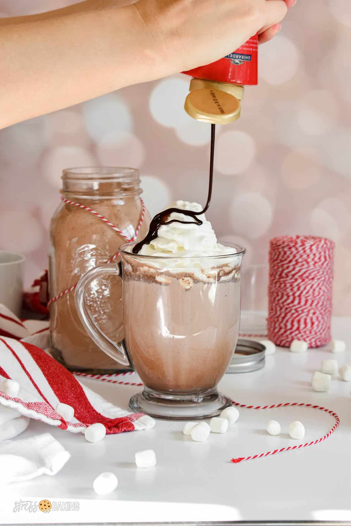 Chocolate syrup being drizzled on top of a mug of hot cocoa topped with whipped cream