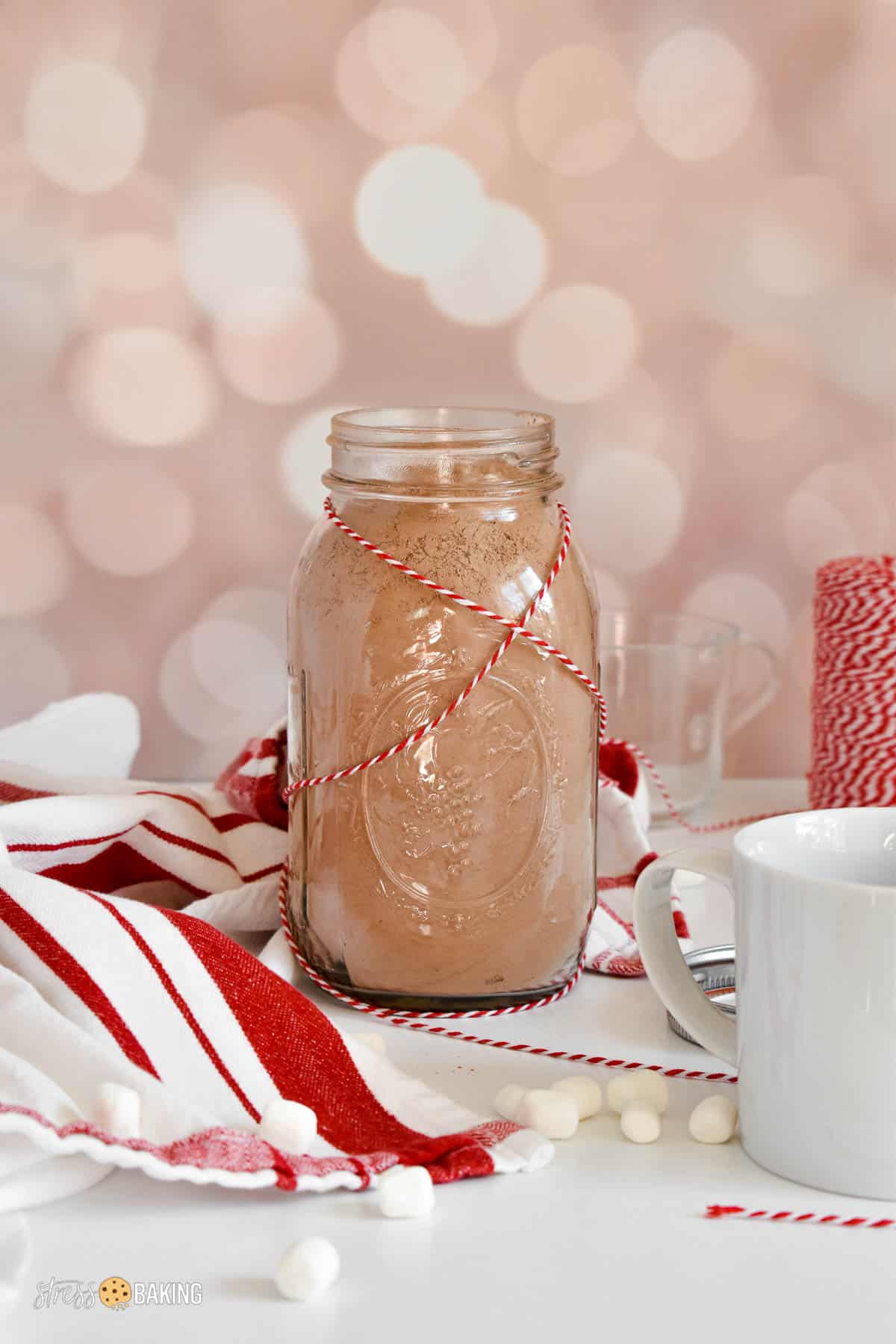 A mason jar full of hot cocoa mix with a festive red and white string around the bottle
