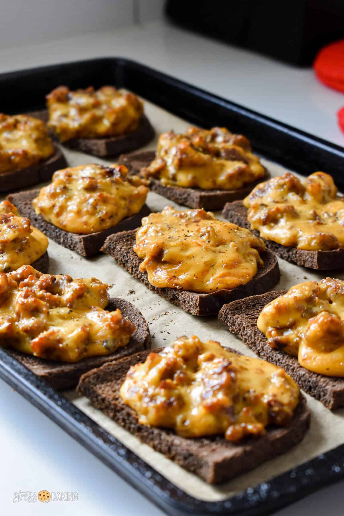 Melted cheese and sausage on slices of pumpernickel bread on a baking sheet