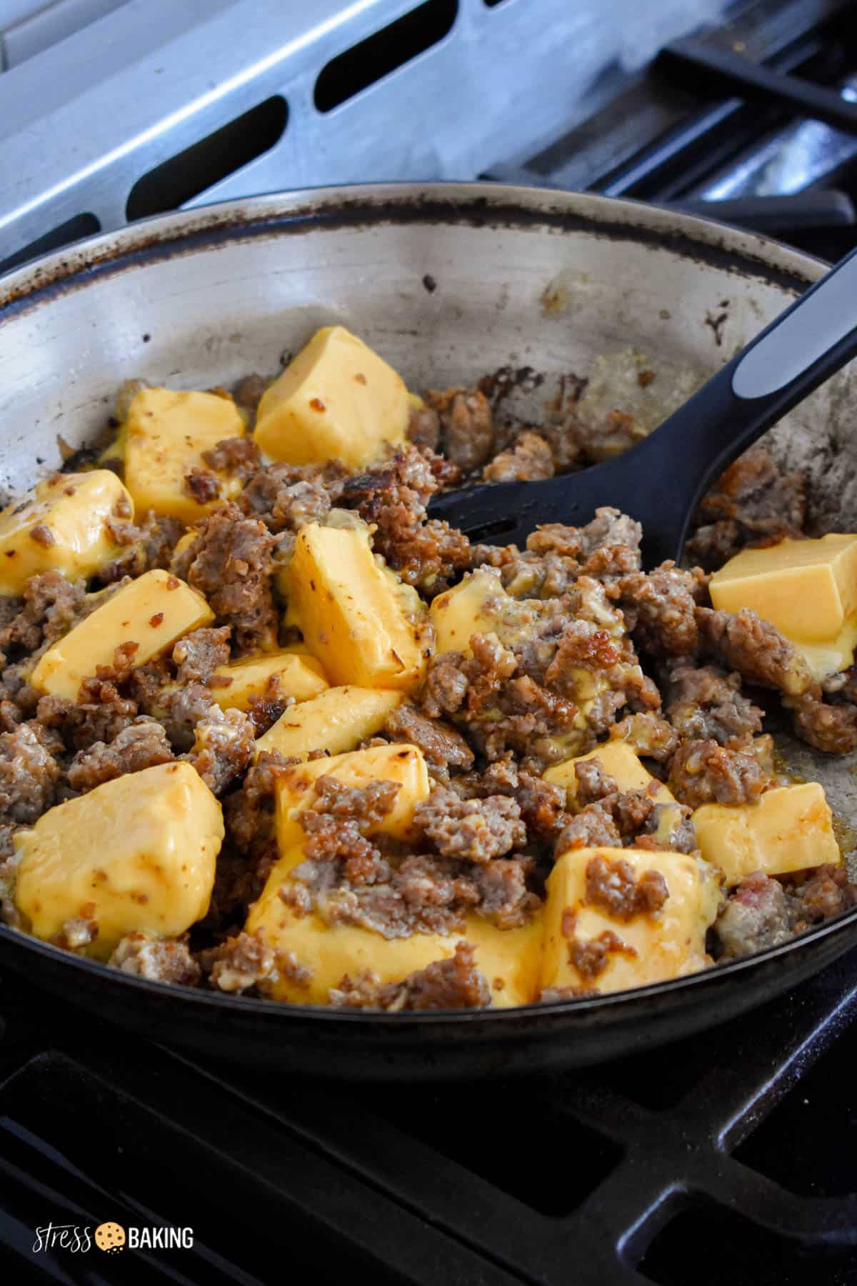 Browned sausage being mixed with Velveeta cheese cubes in a frying pan
