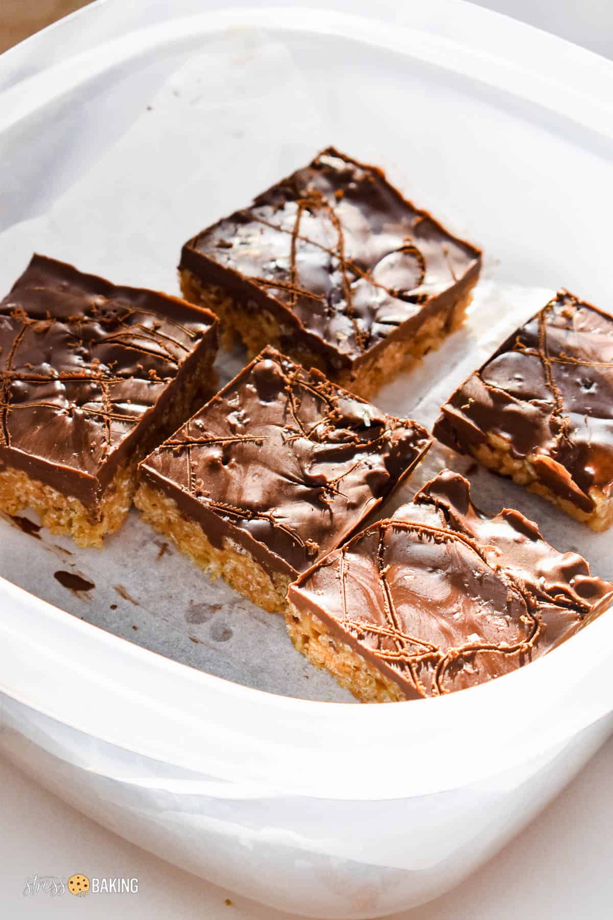 Sliced scotcheroo squares stacked on parchment paper in a clear storage container