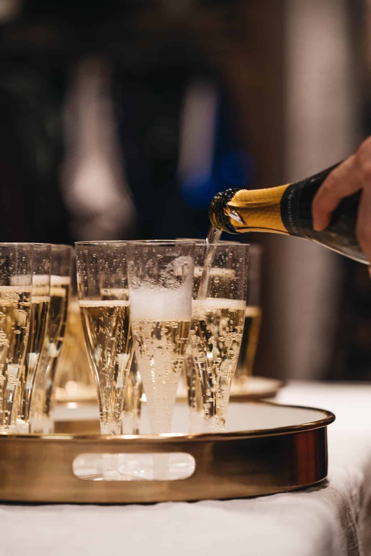 Champagne being poured into glasses on a gold tray