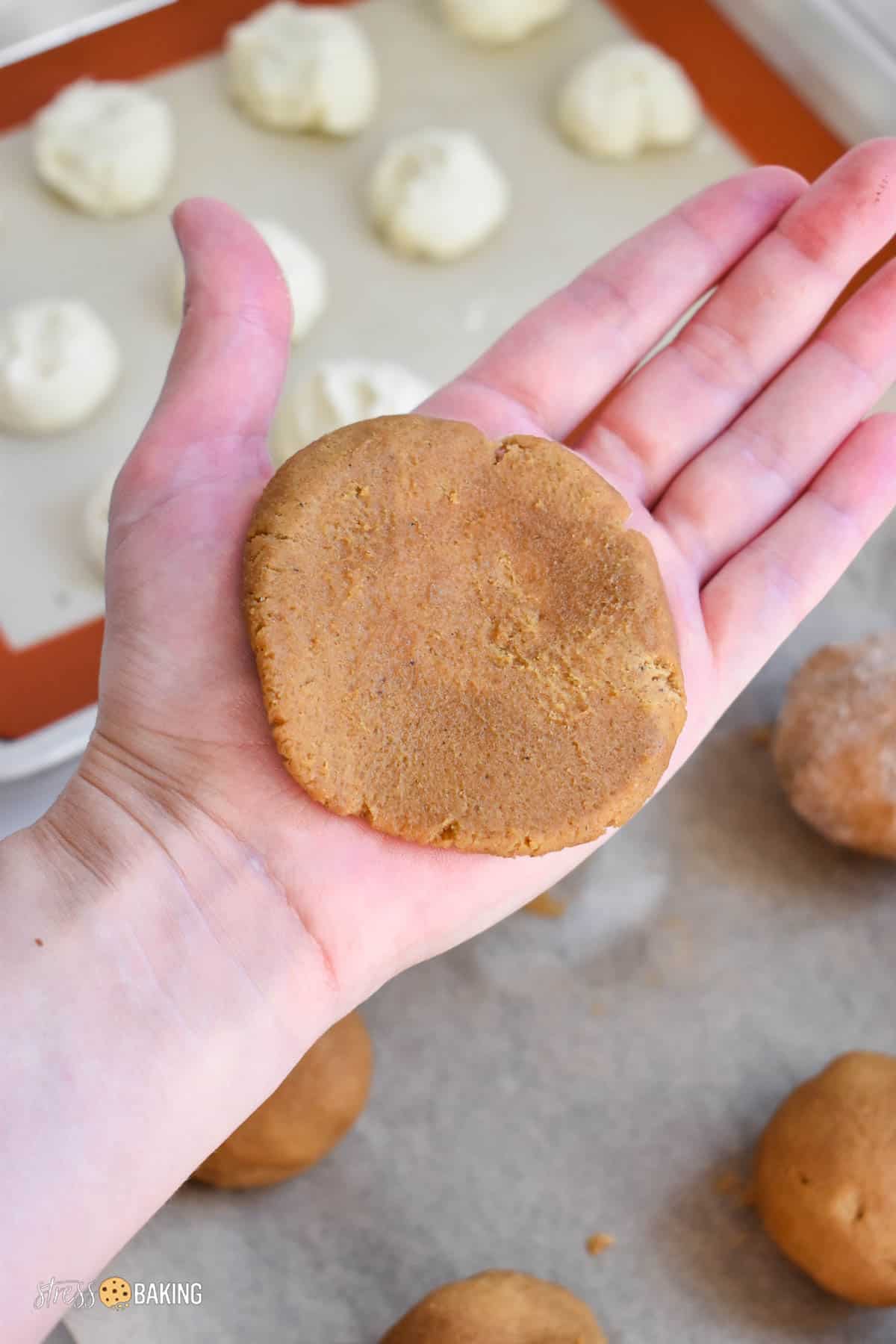 A flattened gingerbread dough ball in the palm of a hand
