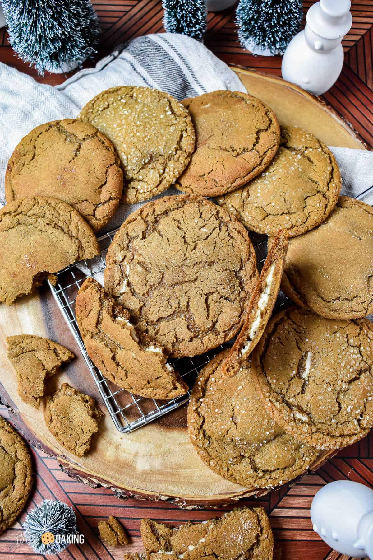 Gingerbread cookies with crinkly tops arranged in a circle on a wood platter with one cookie broken in half to show the cheesecake filling inside