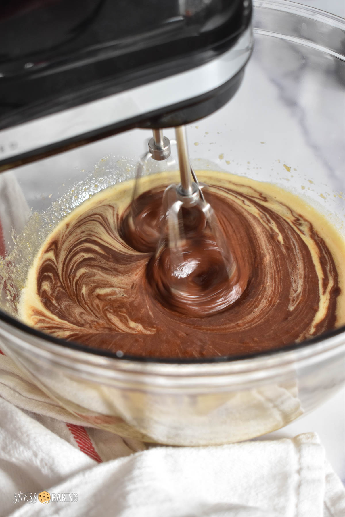 Melted chocolate being mixed into batter with a hand mixer