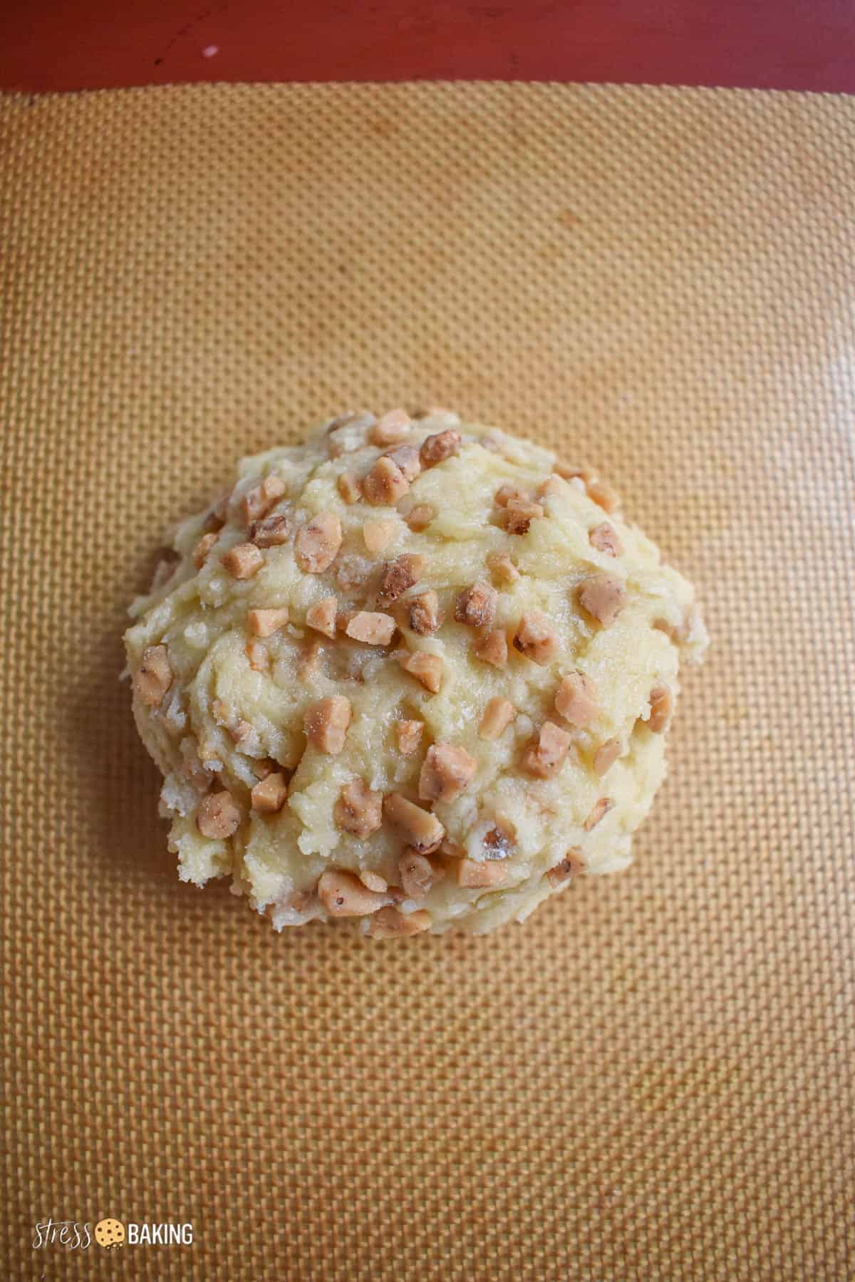 Mound of sugar cookie dough dotted with toffee pieces on a silicone mat