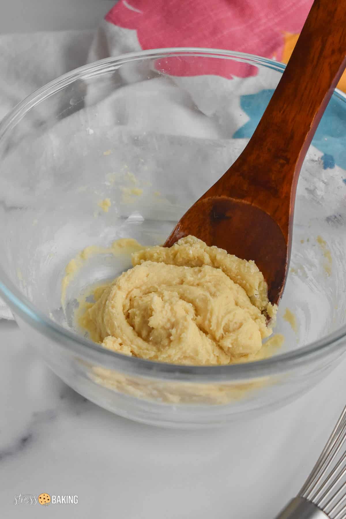 Sugar cookie batter in a glass mixing bowl with a wooden spoon