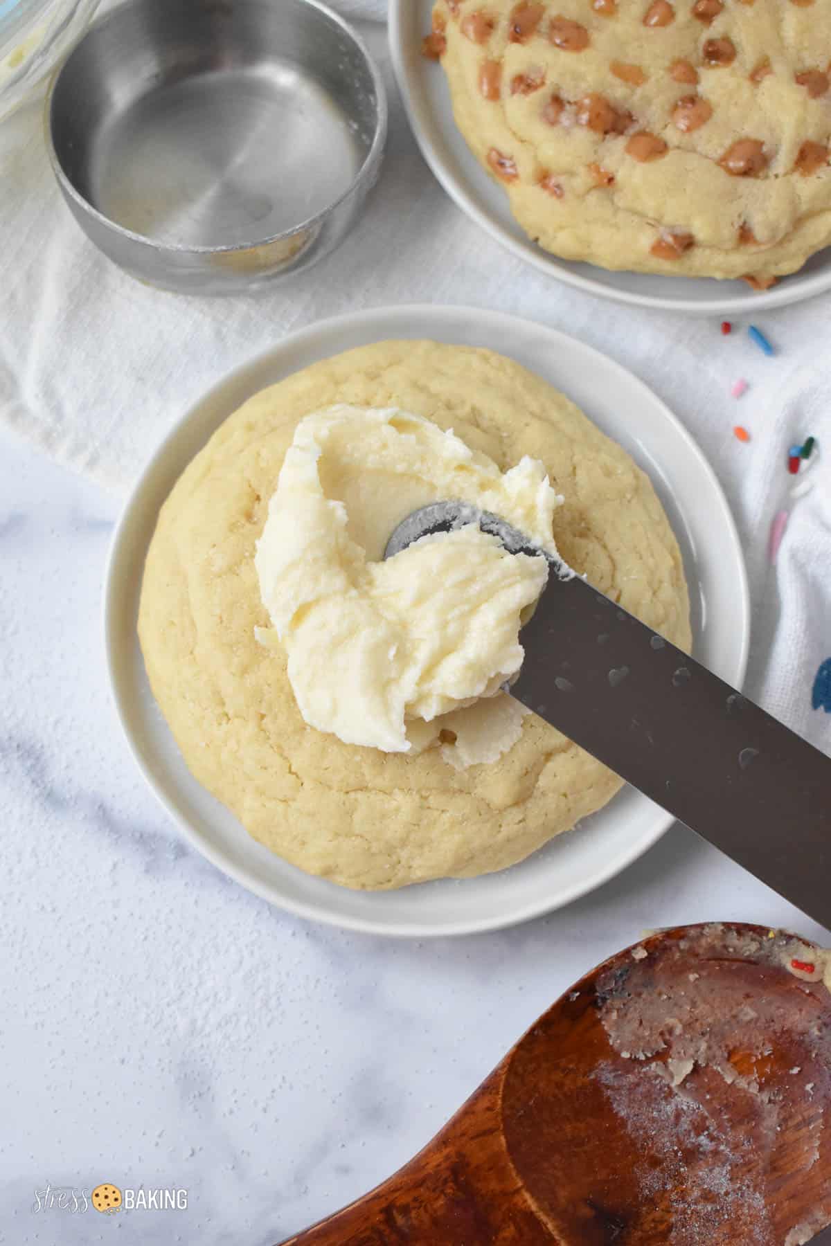 Buttercream frosting being spread on a big sugar cookie with an icing spatula