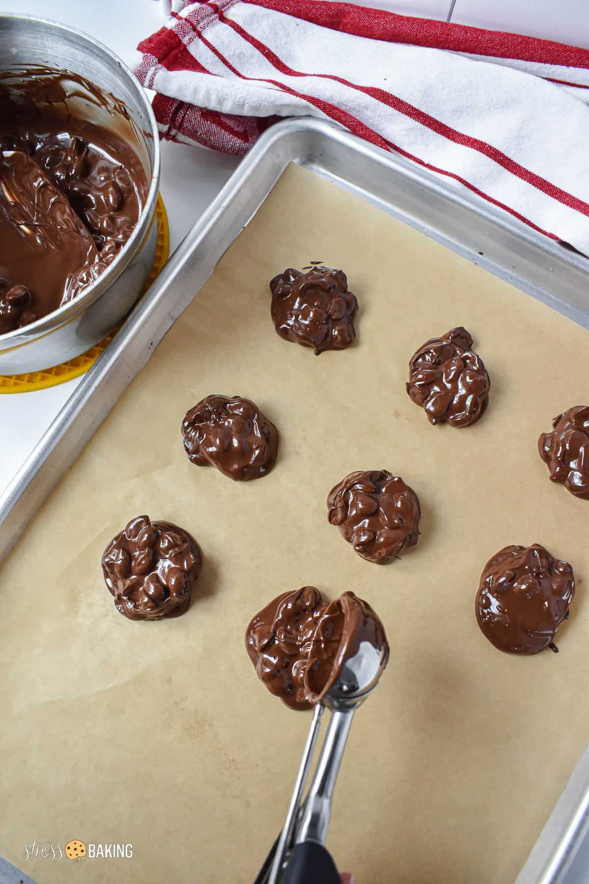 Chocolate covered peanuts being scooped onto a parchment paper-lined baking sheet