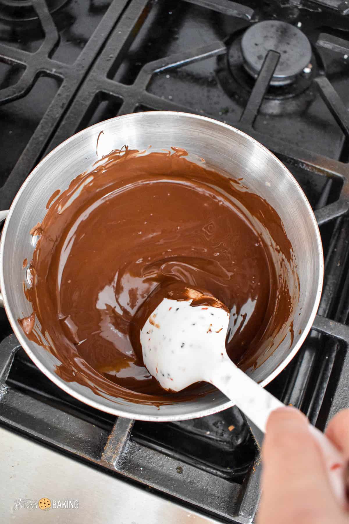 Melted chocolate being stirred with a spatula in a saucepan