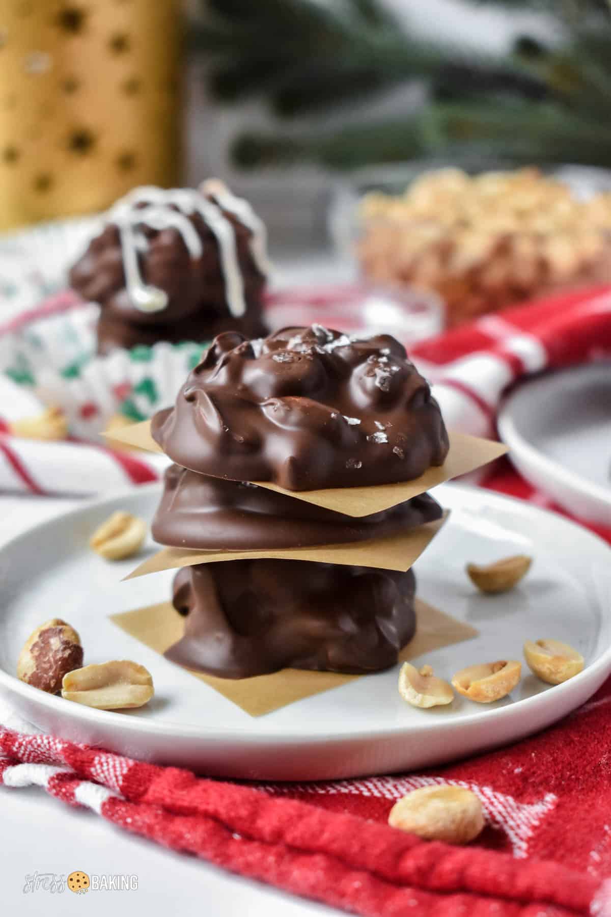 Chocolate covered peanut clusters stacked between pieces of parchment paper on a white plate