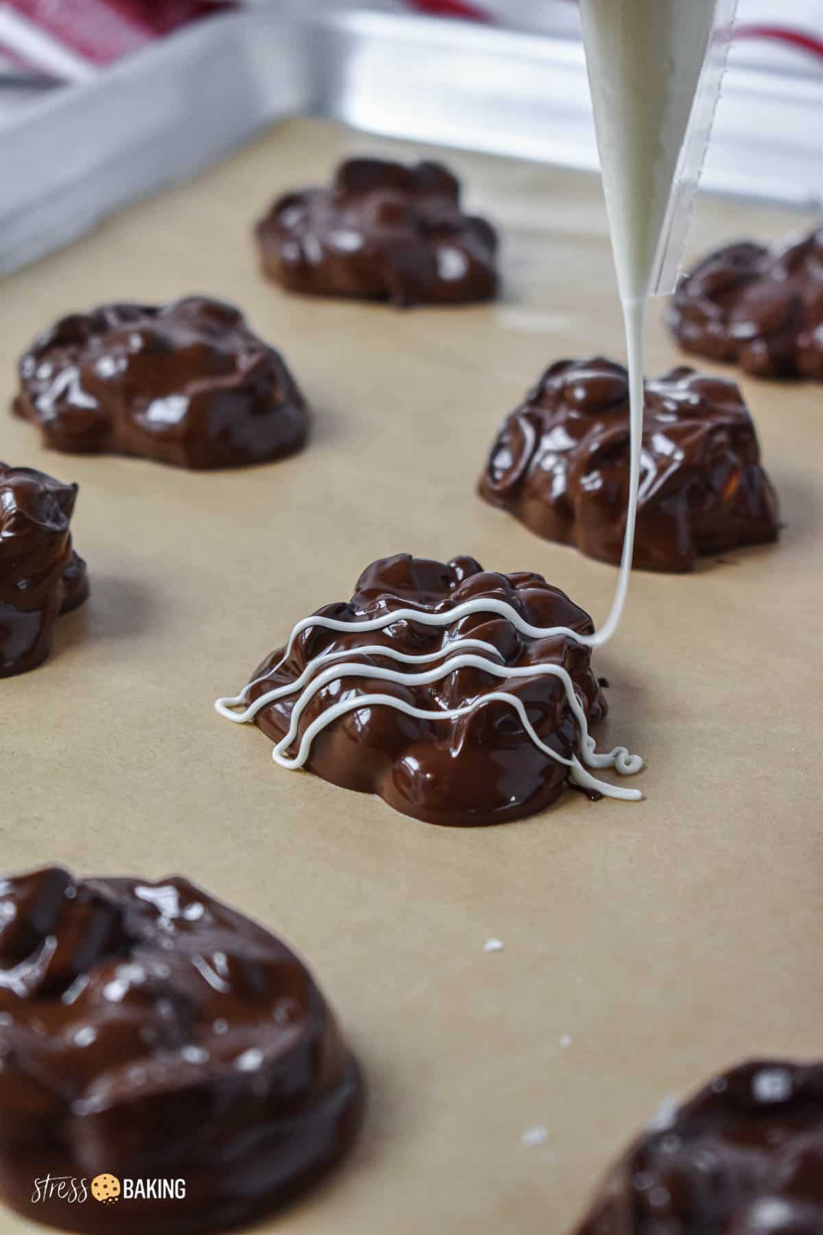 White chocolate being drizzled onto chocolate covered peanut clusters on a parchment paper-lined baking sheet