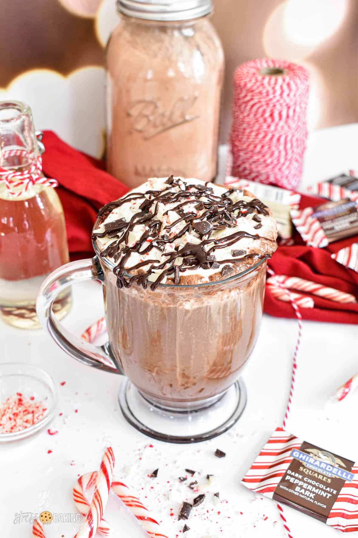 Clear mug of peppermint mocha topped with whipped cream, chopped peppermint bark and a large drizzle of chocolate sauce