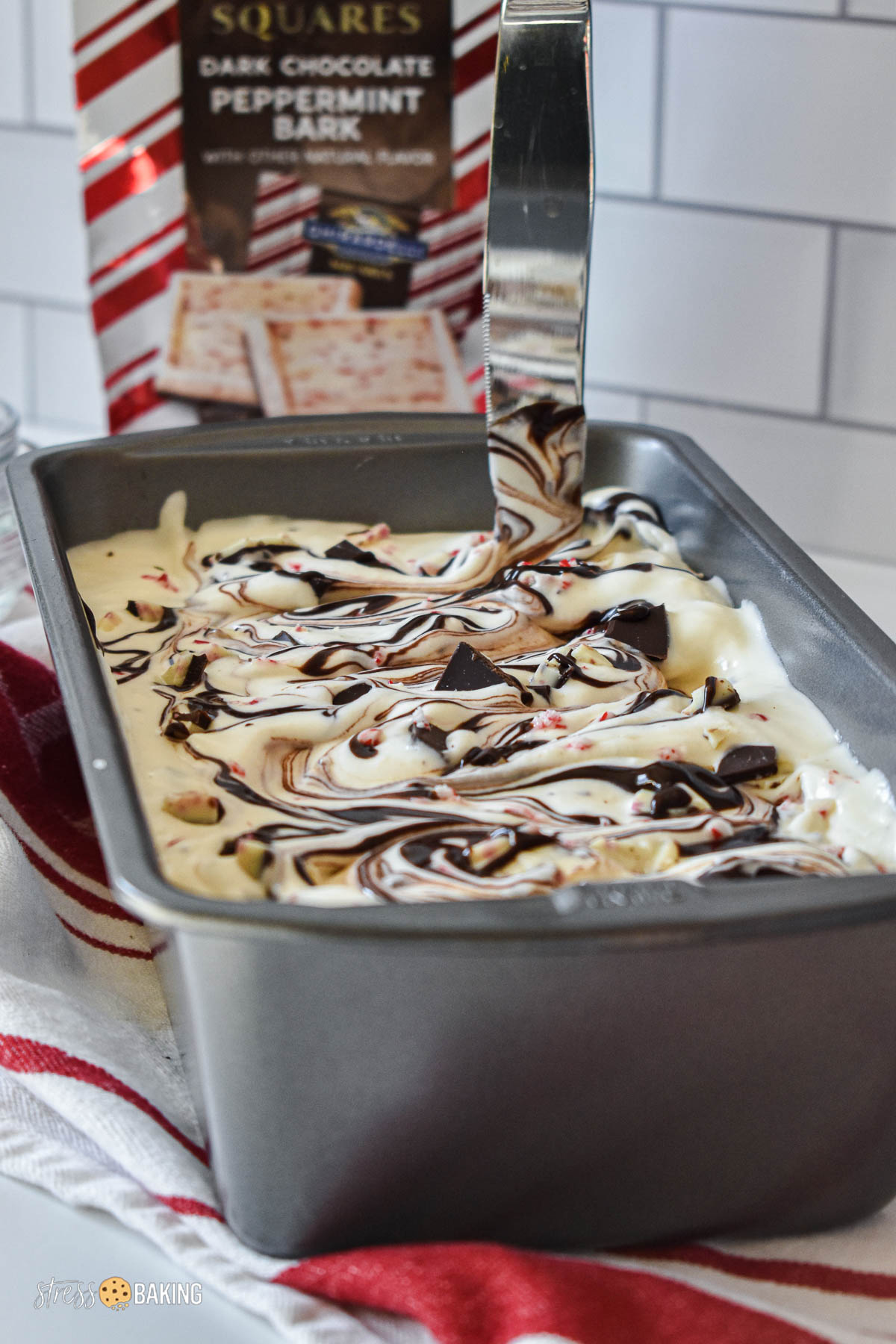 Black and white peppermint bark ice cream in a loaf tin with swirls of chocolate being swirled with a knife