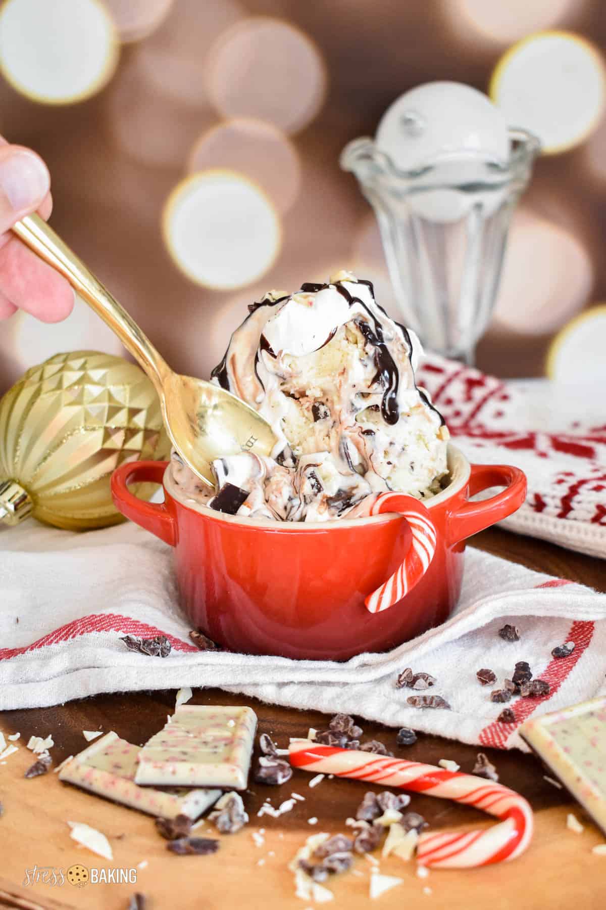 Black and white peppermint bark ice cream topped with whipped cream and chocolate drizzle in a red mini cocotte with a gold spoon taking a scoop