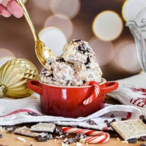 Black and white peppermint bark ice cream in a red mini cocotte with a gold spoon taking a scoop