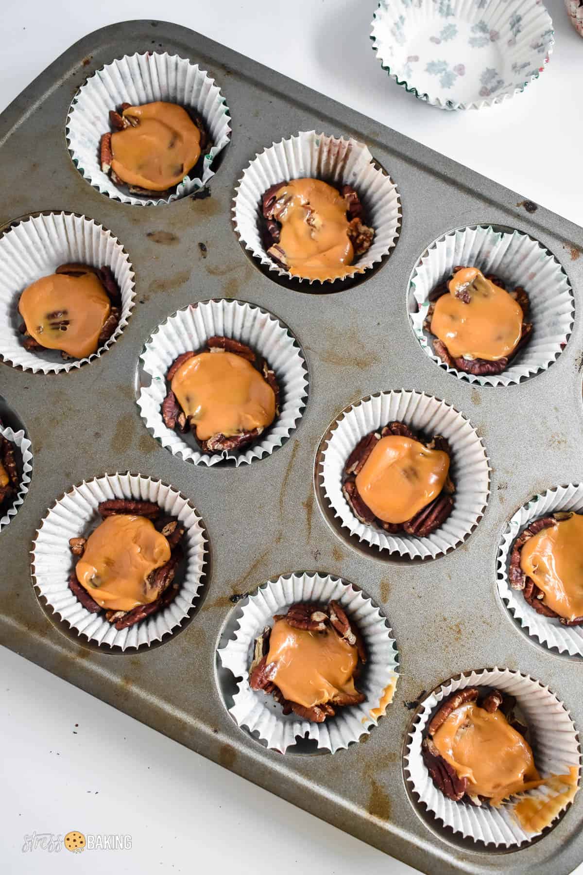 Muffin pin filled with cupcake liners filled with pecan pieces and melted soft caramels