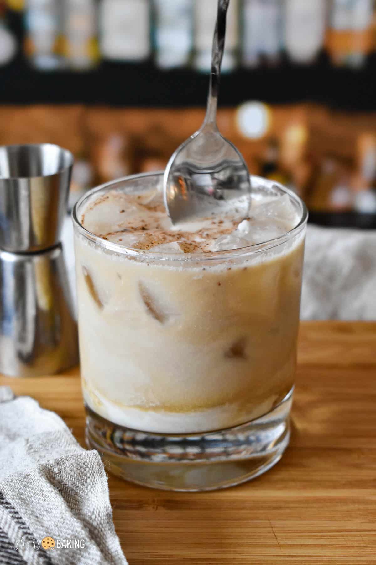 White Russian cocktail being stirred in a clear old fashioned rocks glass on a wood cutting board