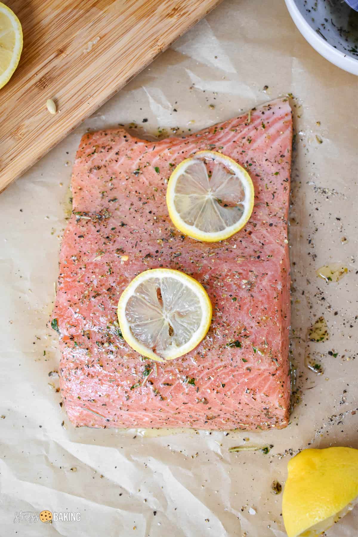 Pink raw salmon filet on parchment paper coated in spices and lemon slices