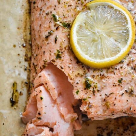 Baked salmon coated in spices and thin lemon slices flaking apart on parchment paper