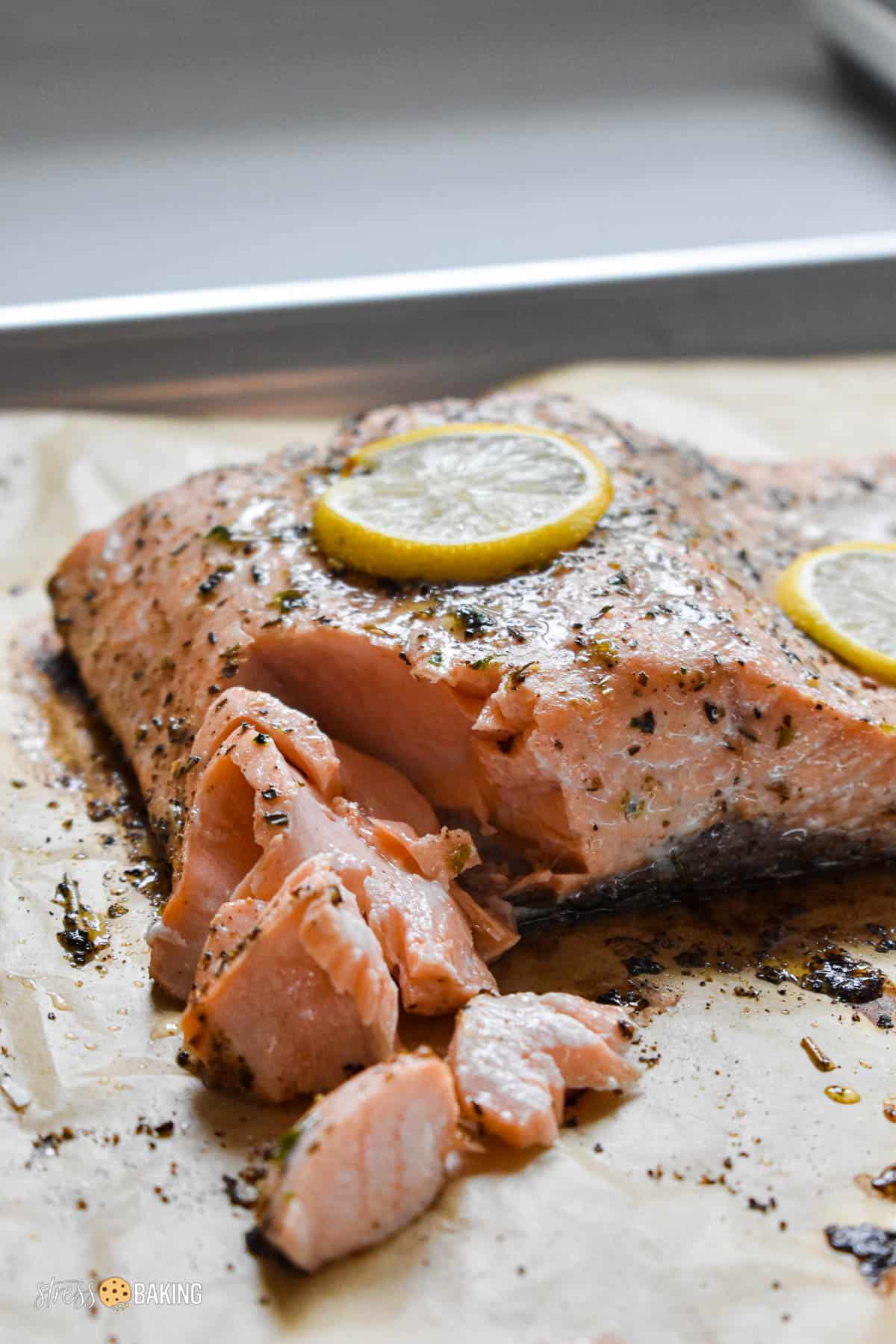 Baked salmon coated in spices and thin lemon slices flaking apart on parchment paper