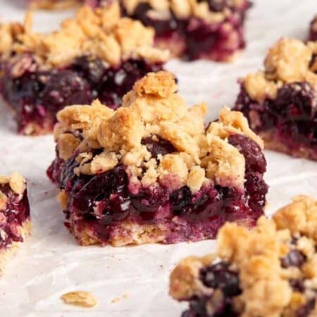Golden oatmeal topping on slices of purple blueberry bars on parchment paper