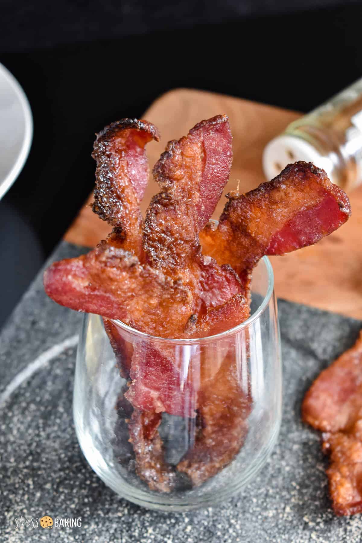Candied bacon strips in a clear glass on a charcoal and wood surface