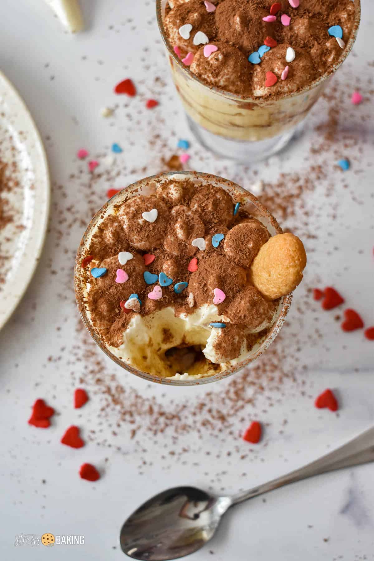 Tiramisu in a trifle dish topped with a dusting of cocoa powder and heart sprinkles with a spoonful removed