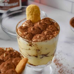 Tiramisu in a trifle dish topped with a dusting of cocoa powder