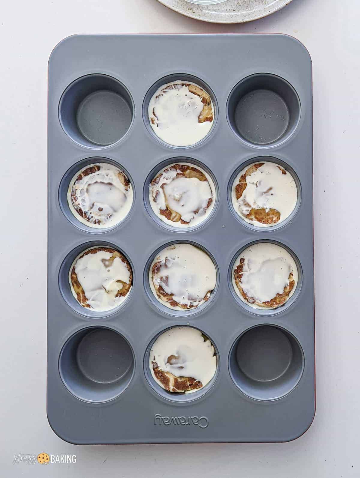 Cinnamon rolls in the muffin cups of a Caraway muffin pan soaked in heavy cream and butter
