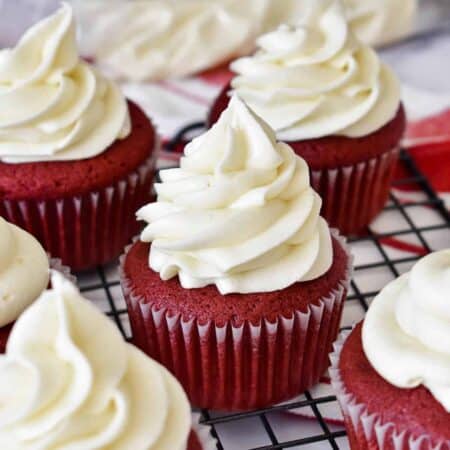 White cream cheese frosting piped high on red velvet cupcakes