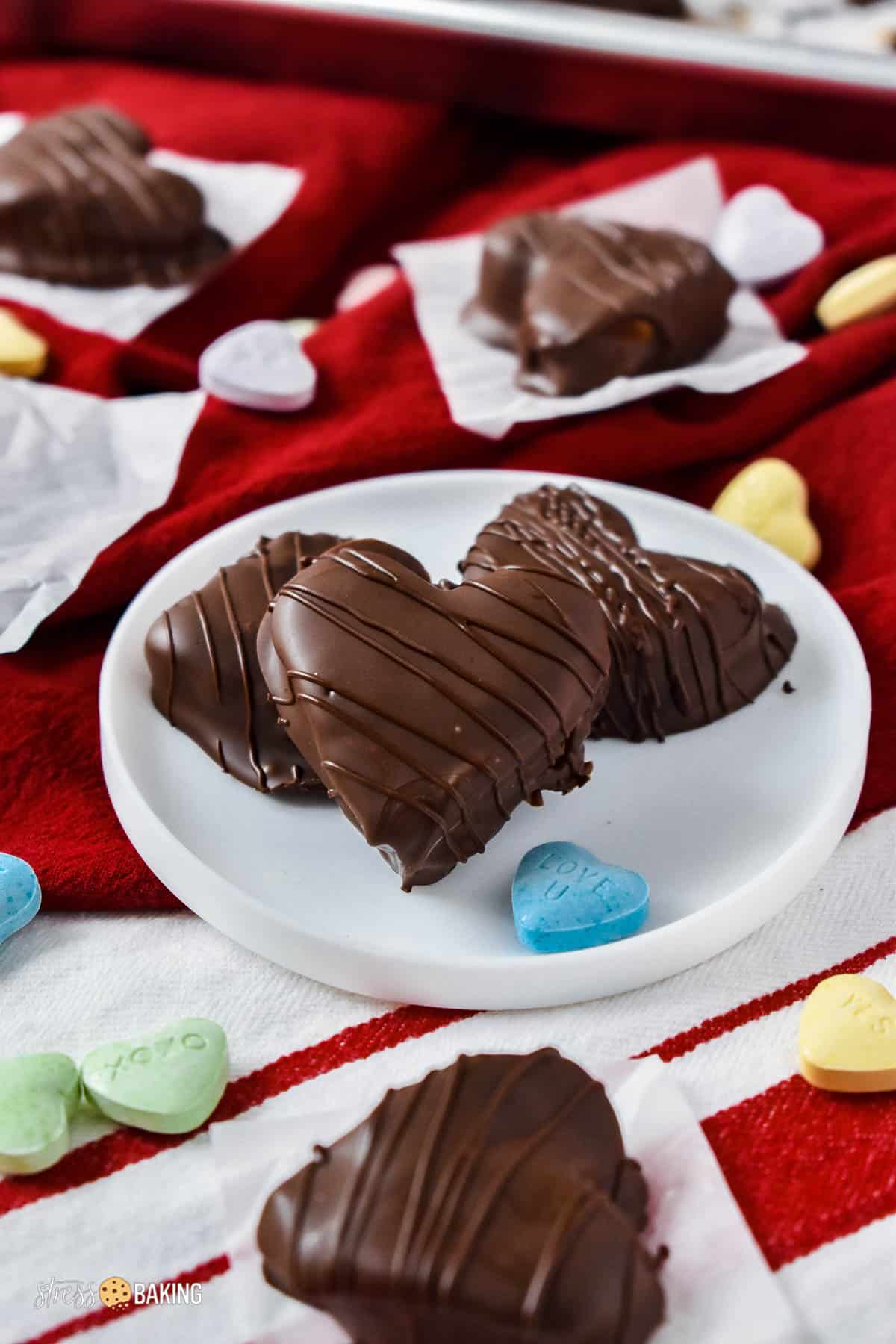 Chocolate covered peanut butter hearts on red and white kitchen towels with multicolored candy hearts
