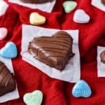 Chocolate covered peanut butter hearts on red and white kitchen towels with multicolored candy hearts