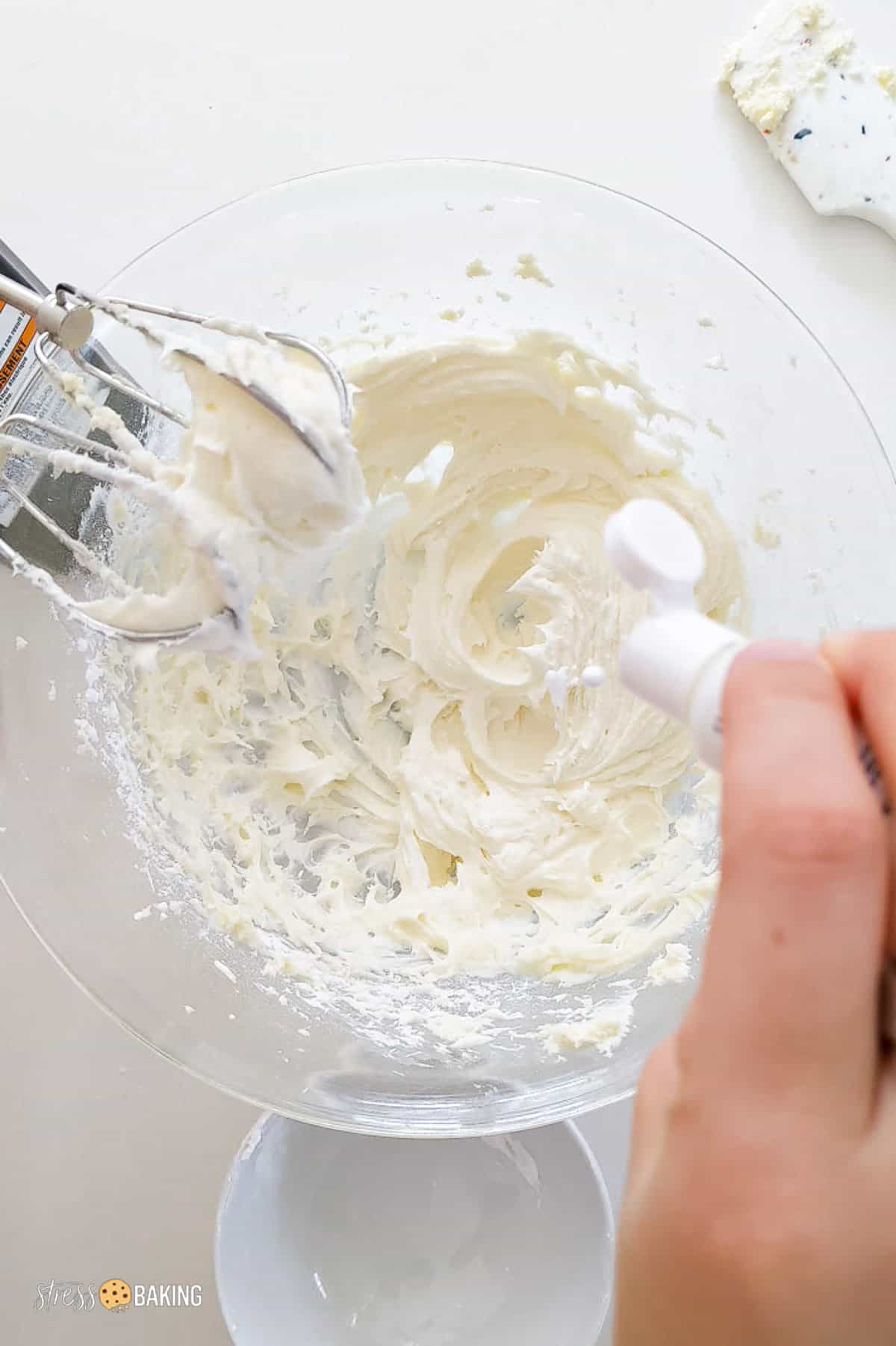 White food gel paste being dropped into a bowl of cream cheese frosting