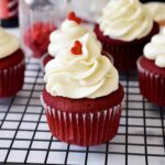 Red velvet cupcake topped with a swirl of cream cheese frosting and a tiny heart sprinkle