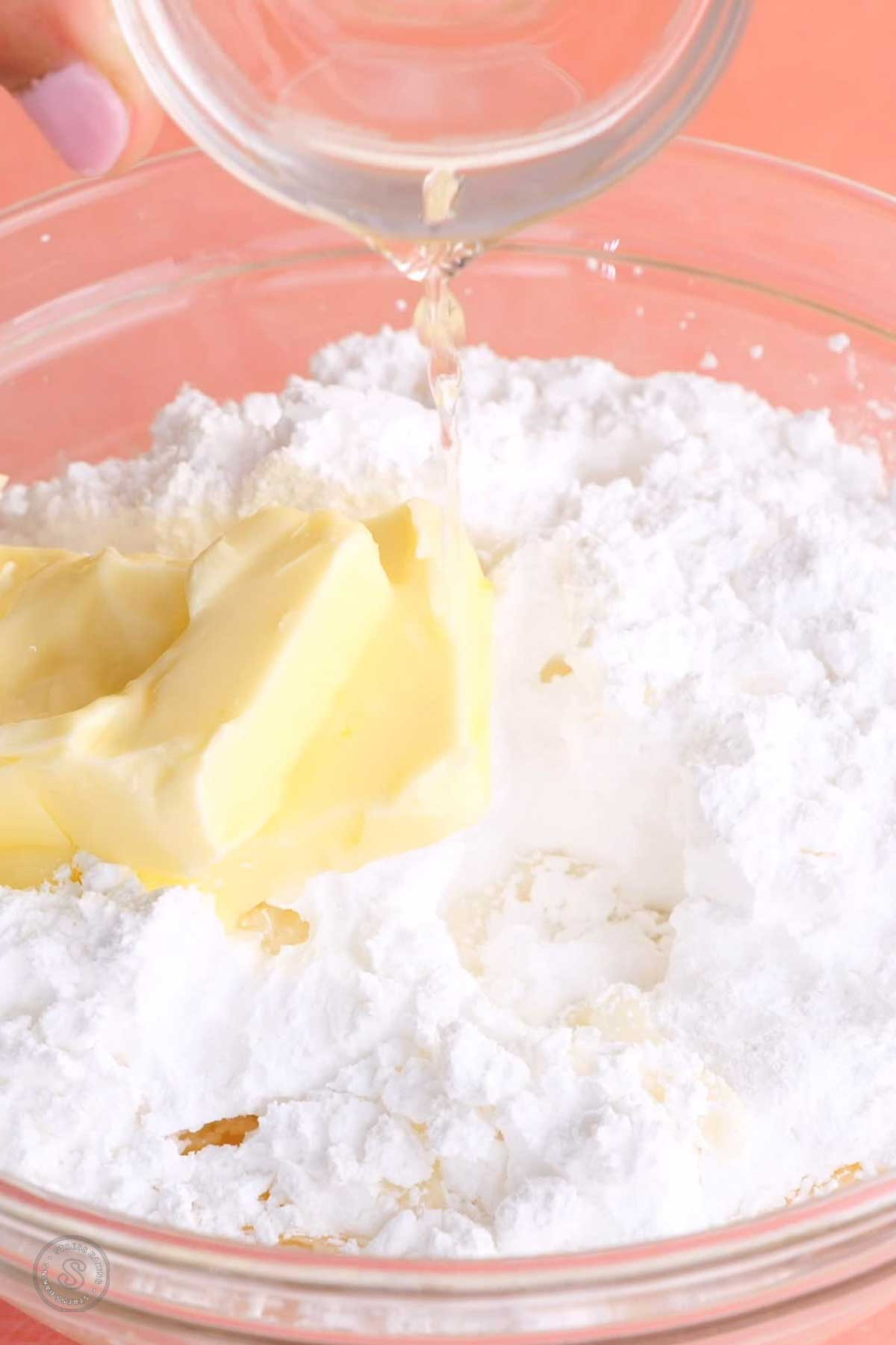 Lemon juice being poured into a bowl of butter and powdered sugar