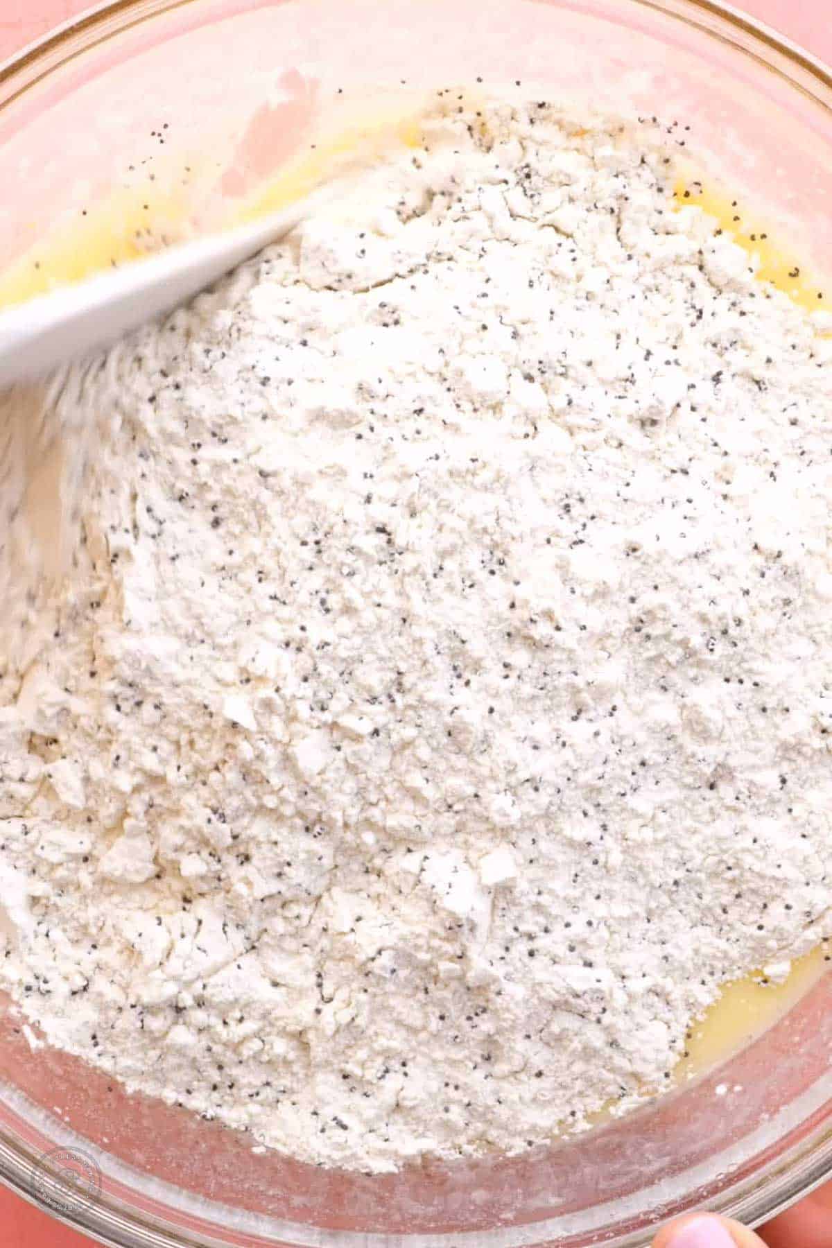 Dry ingredients being folded into a yellow batter with a white spatula