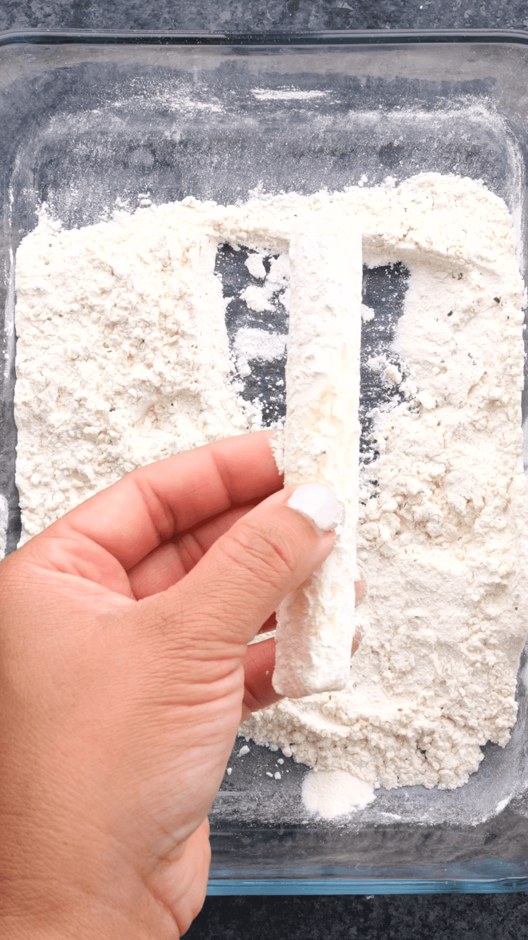 Mozzarella stick being dredged in an flour mixture