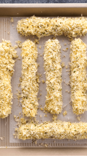 Breaded cheese sticks in a single layer in a baking pan